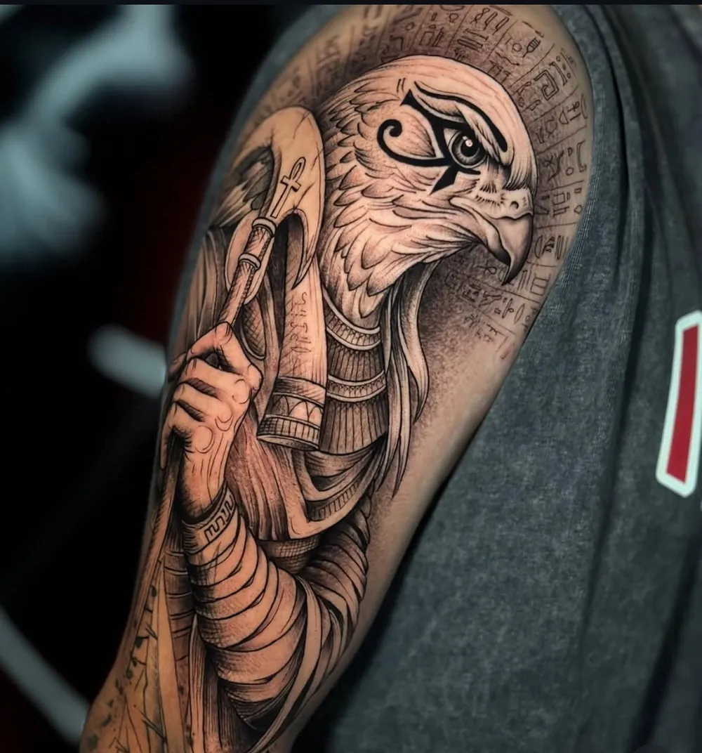 Tatuaje de realismo en el brazo del dios egipcio Horus, con cabeza de halcón, jeroglíficos y un ankh